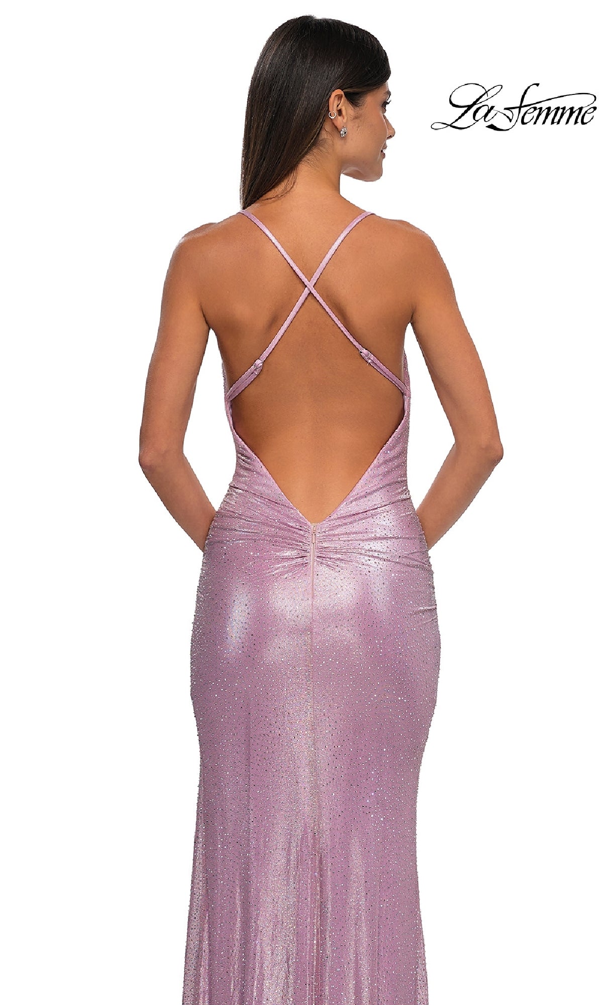 A woman stands facing away in a shimmering light purple Metallic-Jersey Long Prom Dress, La Femme 32835, featuring crisscross straps and an open back.